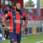 Andy Carroll staat in rood-donkerblauw voetbaltenue naast het veld.