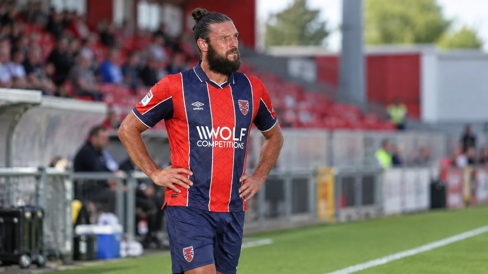 Andy Carroll staat in rood-donkerblauw voetbaltenue naast het veld.