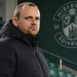 Reedijk in een neutrale jas voor een vast Hibernian-clubembleem in het stadion.