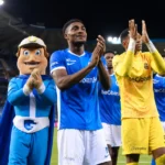 Spelers van KRC Genk en de clubmascotte applaudisseren langs het veld voor de supporters.