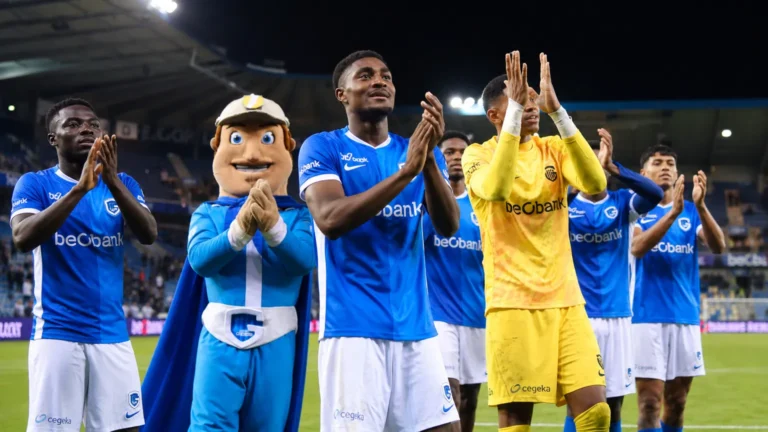 Spelers van KRC Genk en de clubmascotte applaudisseren langs het veld voor de supporters.