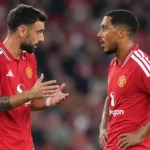 Twee spelers van Manchester United in rode wedstrijdtenues overleggen op het veld.