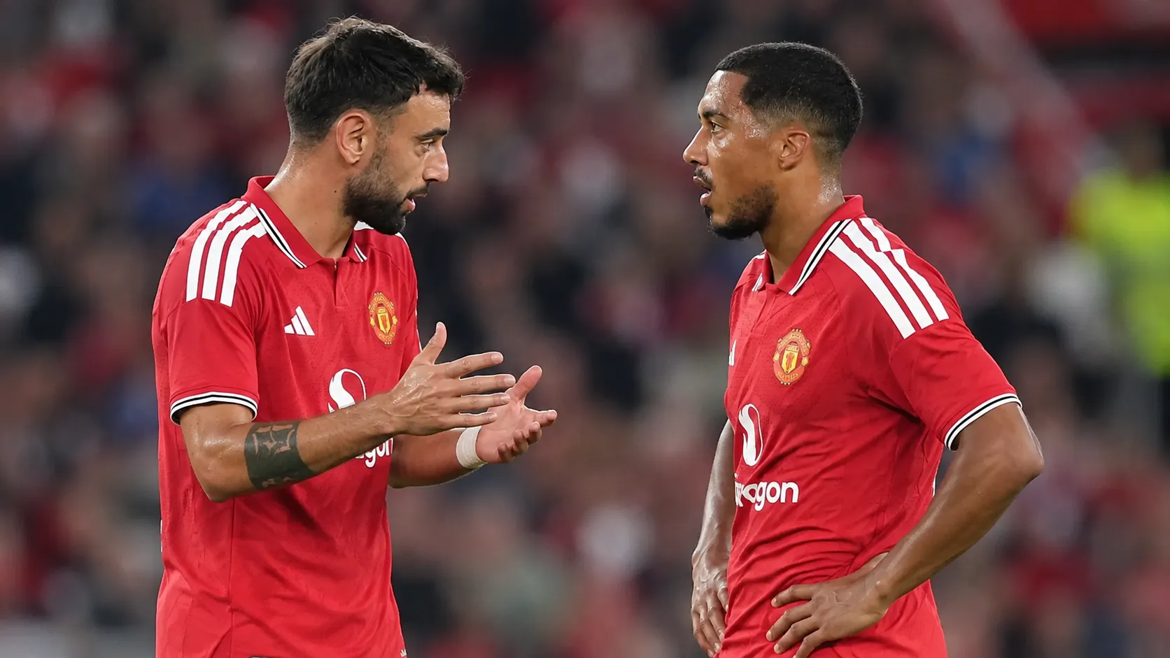 Twee spelers van Manchester United in rode wedstrijdtenues overleggen op het veld.