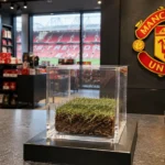 Transparante kubus met oude grasmat op een verkoopdisplay met een Manchester United-embleem aan de wand.