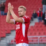 Een speler van Antwerp applaudisseert in een stadion met rode zitjes.