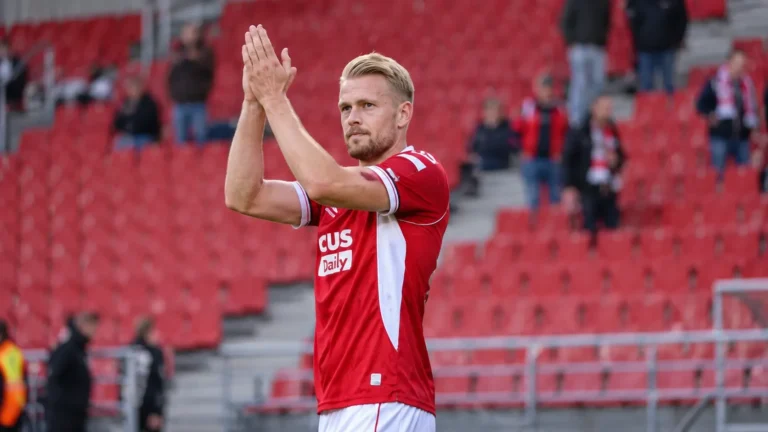 Een speler van Antwerp applaudisseert in een stadion met rode zitjes.