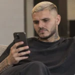 Mauro Icardi kijkt naar een smartphone in een neutrale binnenruimte.