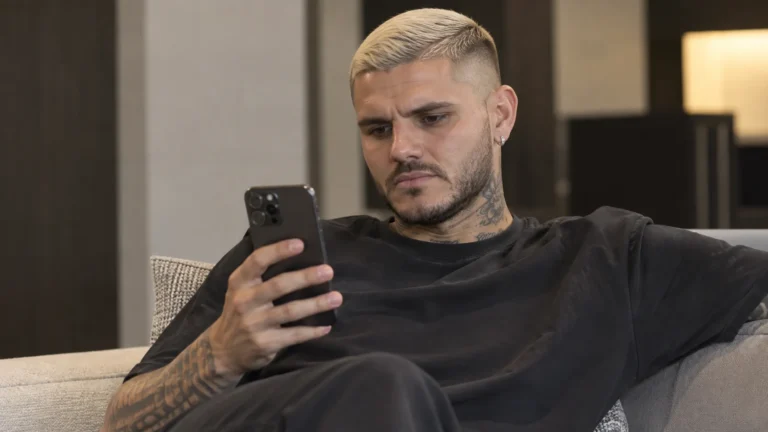 Mauro Icardi kijkt naar een smartphone in een neutrale binnenruimte.