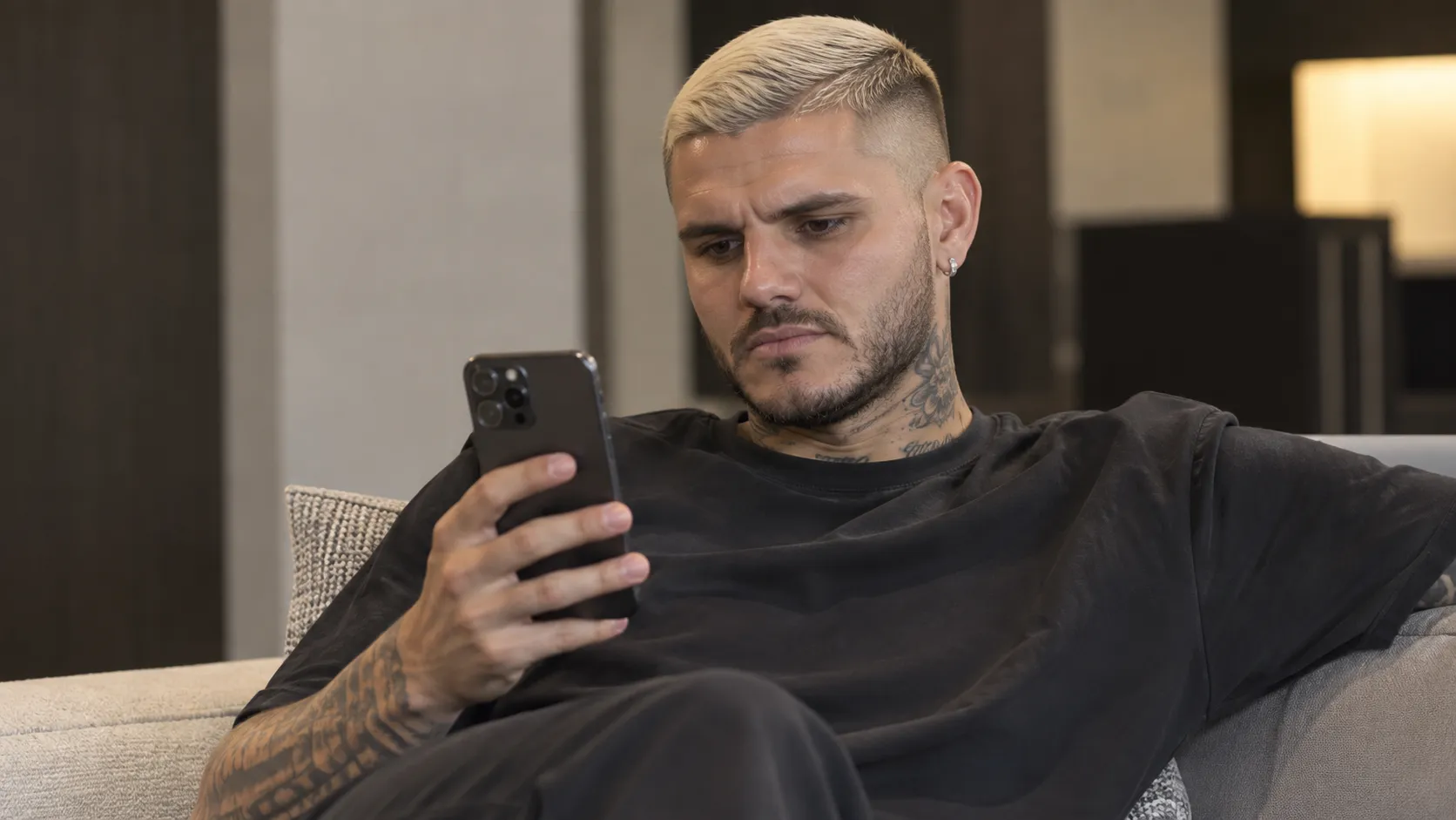 Mauro Icardi kijkt naar een smartphone in een neutrale binnenruimte.
