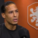 Virgil van Dijk beantwoordt een vraag in een neutrale mediazone met een Nederlands elftalembleem op de wand.