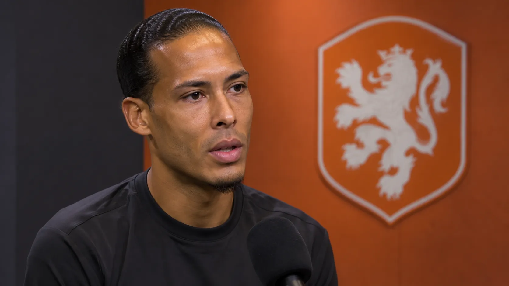Virgil van Dijk beantwoordt een vraag in een neutrale mediazone met een Nederlands elftalembleem op de wand.