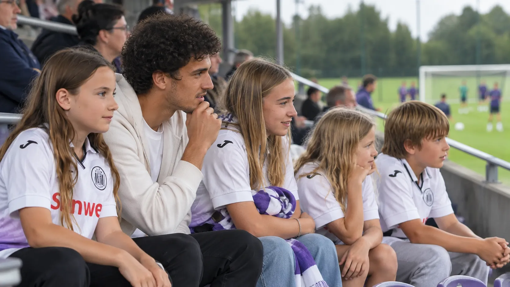 Een groep jonge Anderlecht-supporters met een volwassen begeleider op de tribune.