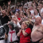 Een dicht opeengepakte groep Engelse voetbalsupporters op een volle tribune.