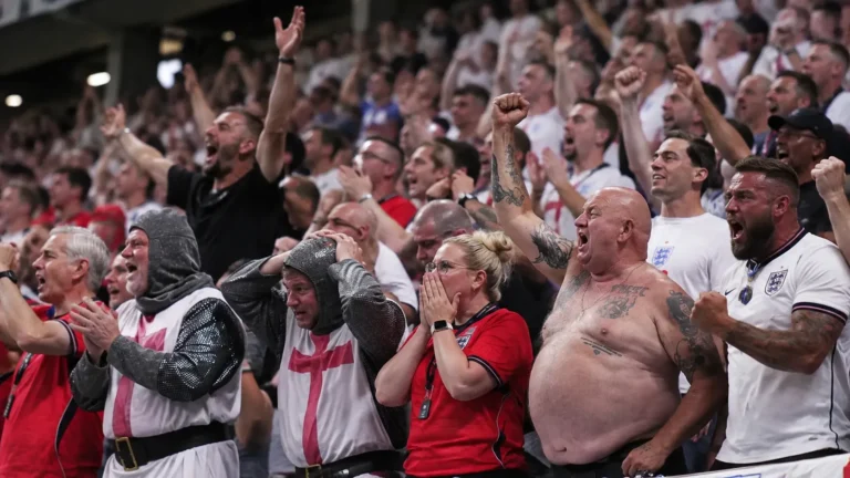 Een dicht opeengepakte groep Engelse voetbalsupporters op een volle tribune.