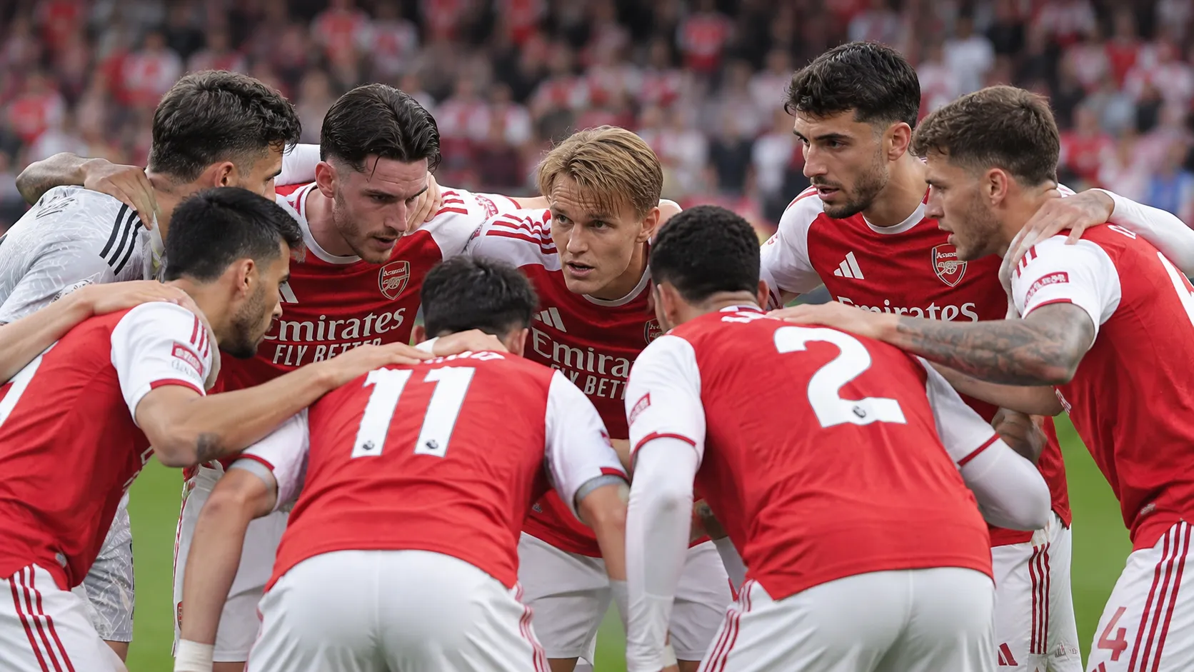 Een groep spelers in rood-witte tenues vormt een huddle op het veld.