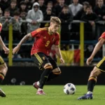 Drie Belgische U21-spelers in rode tenues tijdens een wedstrijdmoment voor enthousiaste supporters.