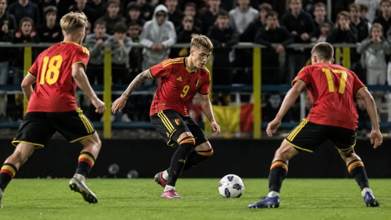 Drie Belgische U21-spelers in rode tenues tijdens een wedstrijdmoment voor enthousiaste supporters.
