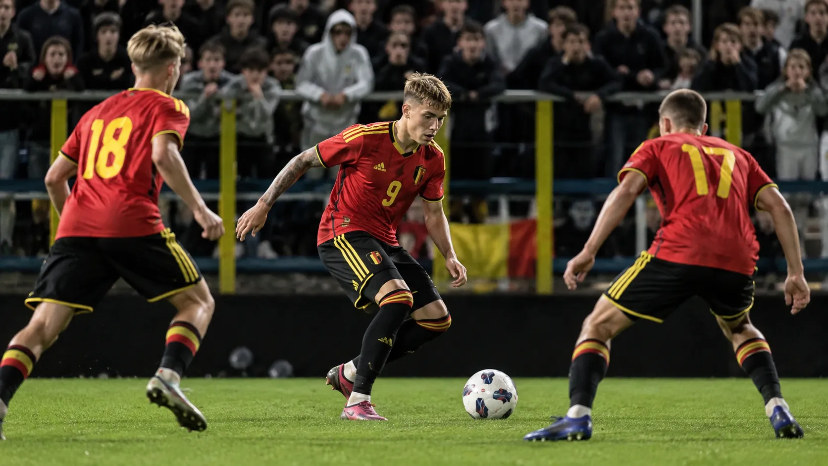 Drie Belgische U21-spelers in rode tenues tijdens een wedstrijdmoment voor enthousiaste supporters.