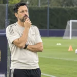 Een coach staat naast een leeg trainingsveld van Anderlecht met trainingsmateriaal op de voorgrond.