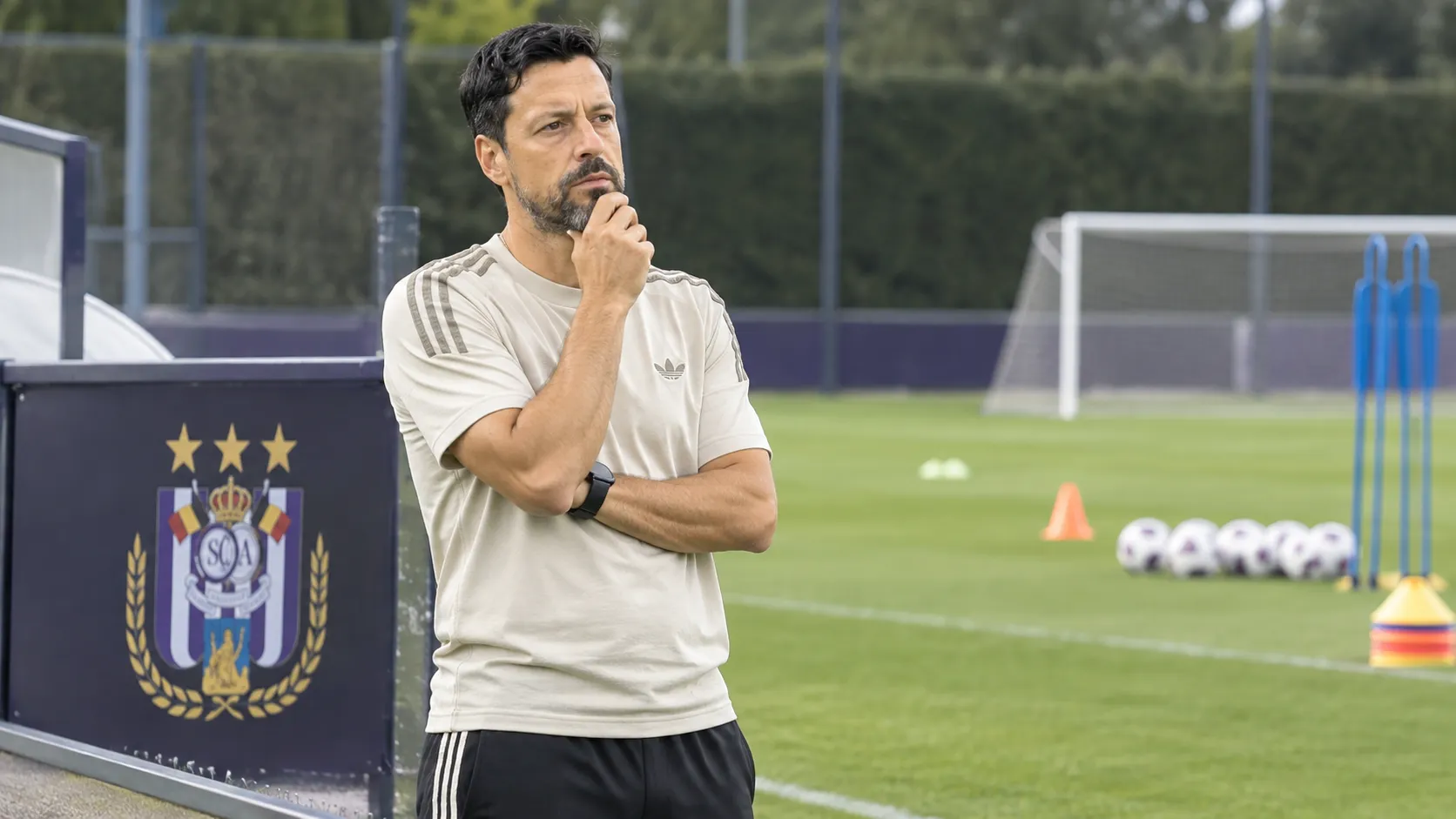 Een coach staat naast een leeg trainingsveld van Anderlecht met trainingsmateriaal op de voorgrond.