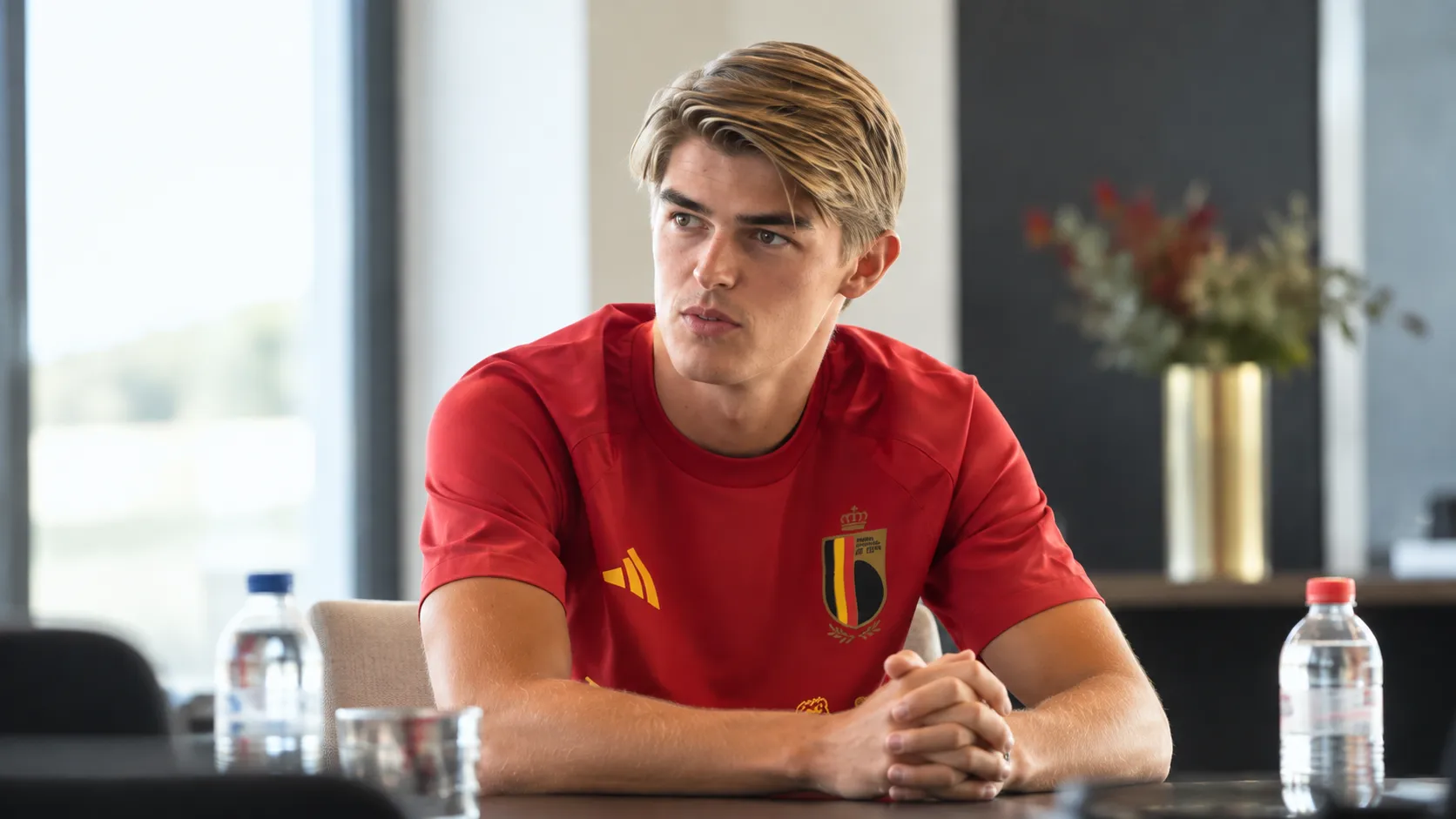 Charles De Ketelaere in het rode shirt van de Belgische nationale ploeg aan een interviewtafel.
