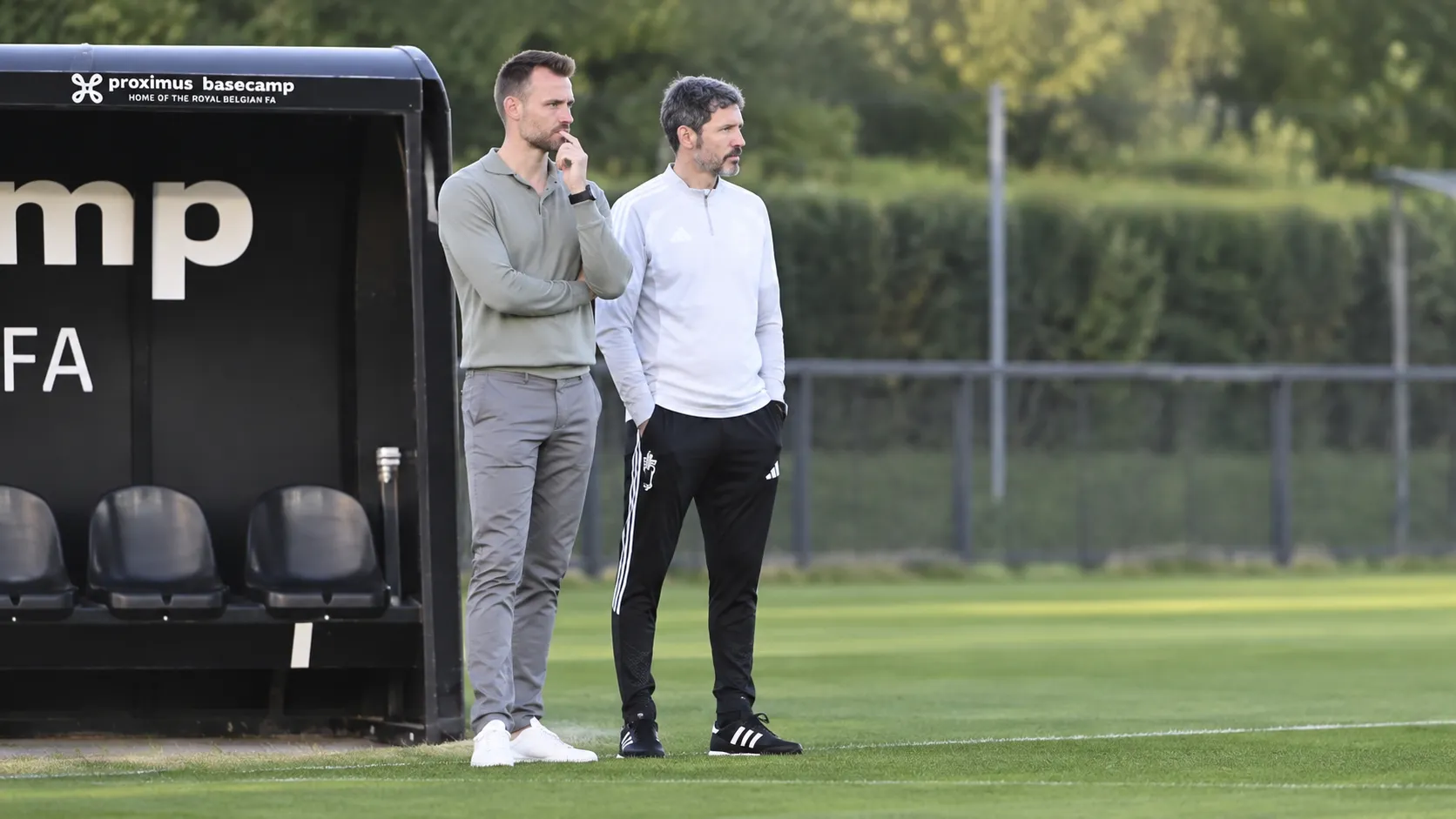 Twee stafleden staan naast de dug-out van het Proximus Basecamp.