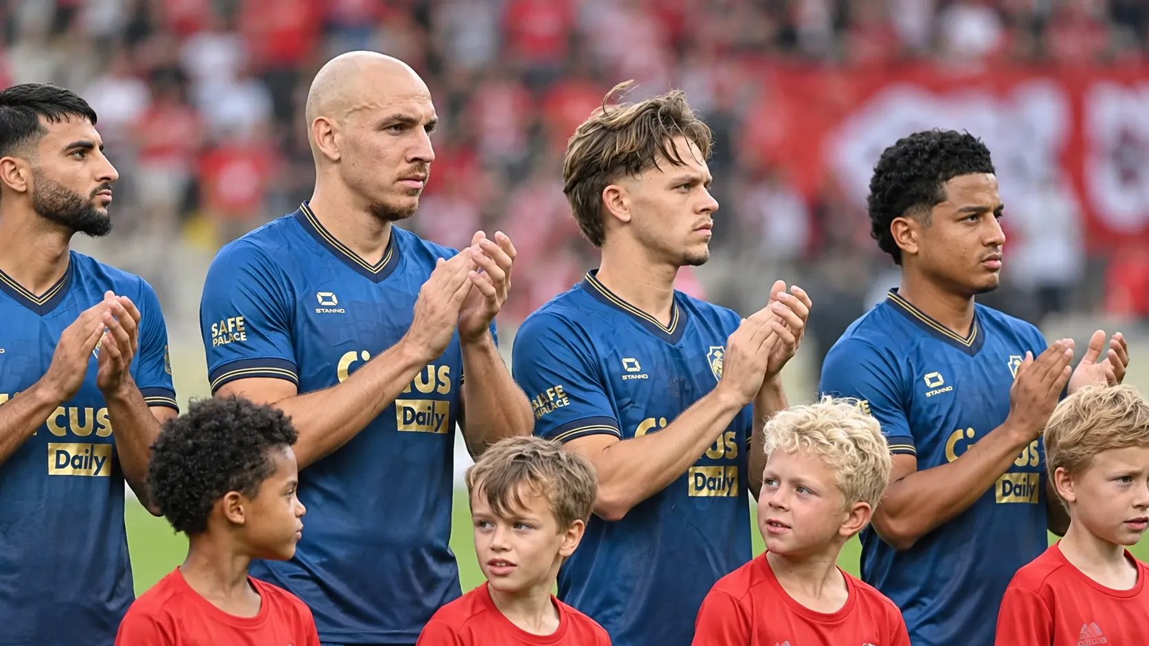 Een groep spelers van Royal Antwerp FC in blauwe wedstrijdshirts met jonge mascottes op het veld.