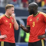 Twee ervaren Belgische internationals in rood tenue overleggen op het veld.