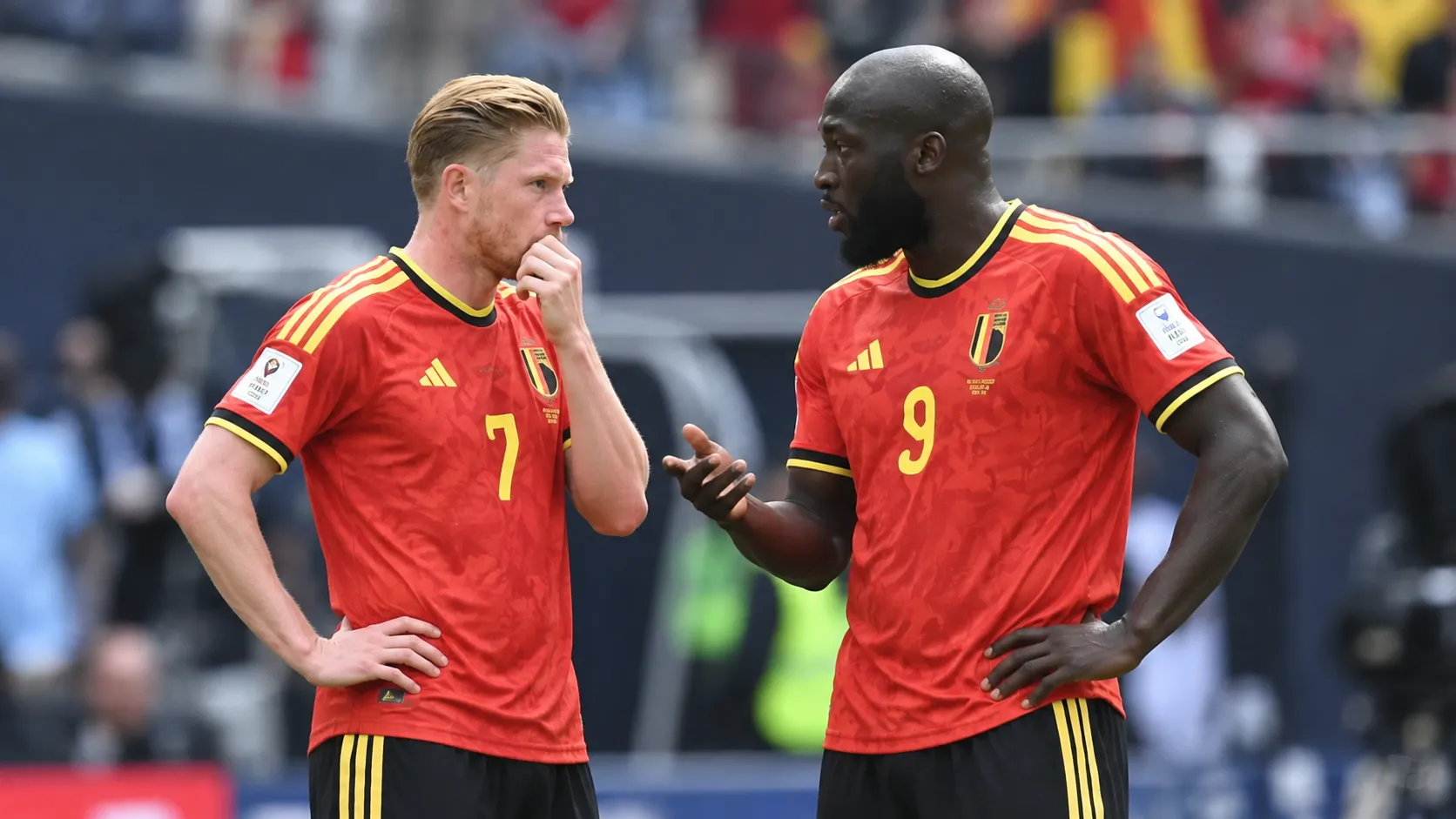 Twee ervaren Belgische internationals in rood tenue overleggen op het veld.