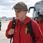 Charles De Ketelaere in een rode trainingsjas van de Rode Duivels op een luchthaven.