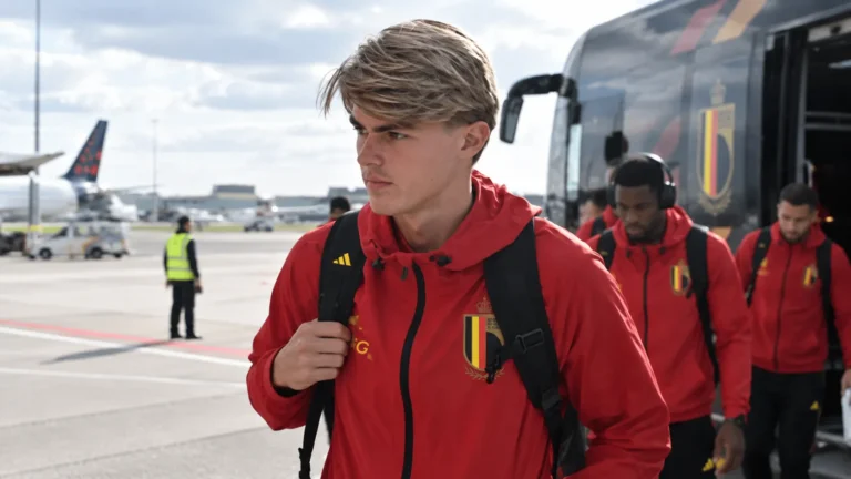 Charles De Ketelaere in een rode trainingsjas van de Rode Duivels op een luchthaven.