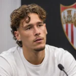 Lucas Stassin tijdens een interview in een ruimte van Sevilla met een clubembleem op de wand.
