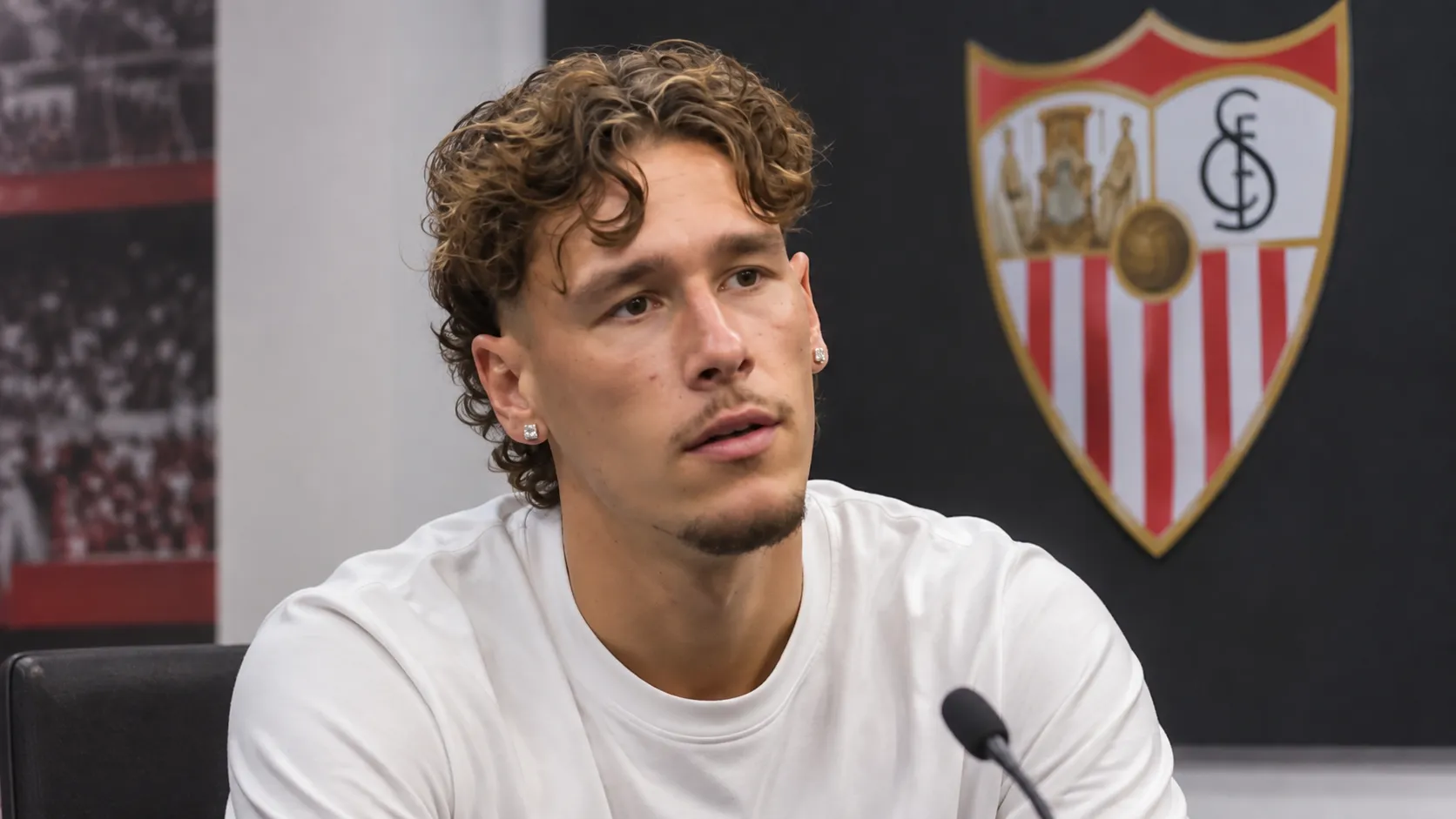 Lucas Stassin tijdens een interview in een ruimte van Sevilla met een clubembleem op de wand.