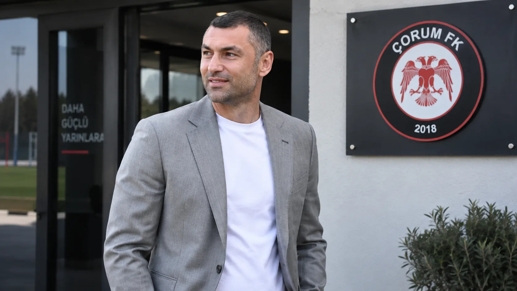 Burak Yilmaz voor het trainingscomplex van Çorum FK met het clubembleem bij de ingang.