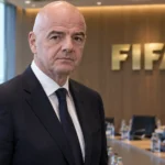 Gianni Infantino in donker pak in een FIFA-bestuursruimte met een FIFA-embleem aan de wand.