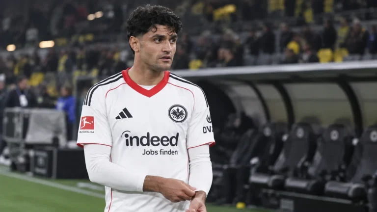 Mahmoud Dahoud in een wit wedstrijdshirt aan de zijlijn van een voetbalstadion.