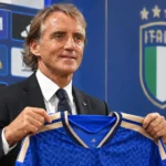 Roberto Mancini houdt een blauw Italië-shirt vast tijdens een persmoment.