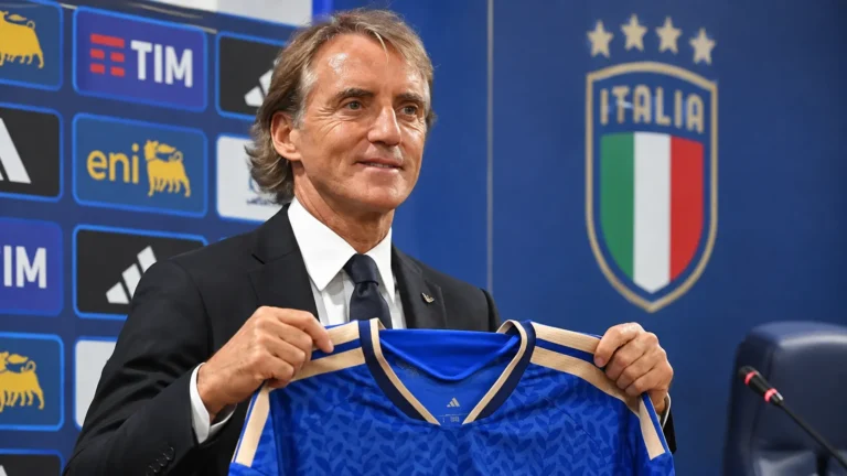 Roberto Mancini houdt een blauw Italië-shirt vast tijdens een persmoment.