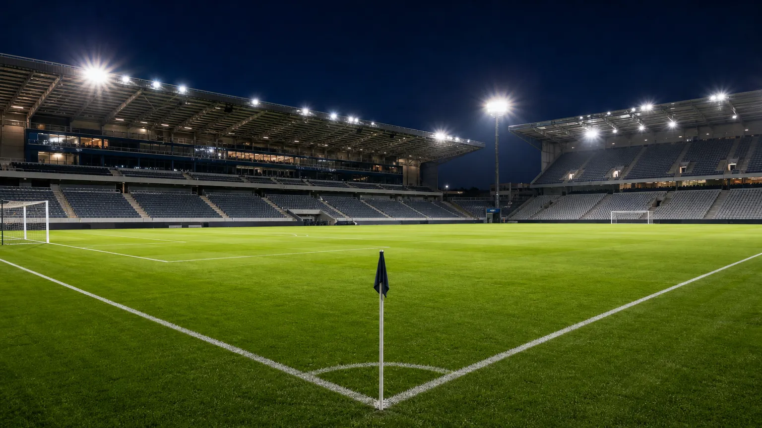Een leeg verlicht voetbalstadion bij avond, met het speelveld en de tribunes in beeld.