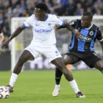 Een speler van Genk dribbelt met de bal tijdens een wedstrijd, met tegenstanders vlakbij.