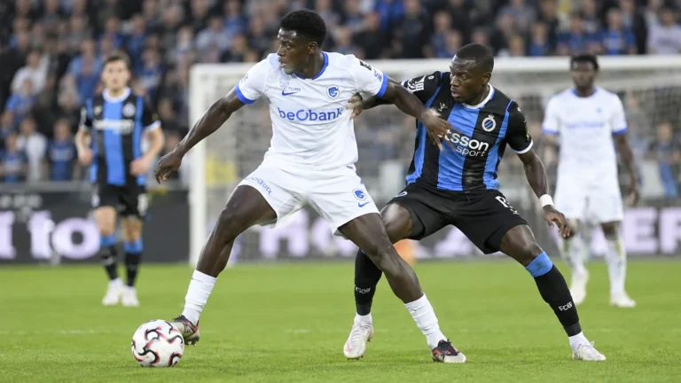 Een speler van Genk dribbelt met de bal tijdens een wedstrijd, met tegenstanders vlakbij.