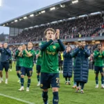Een groep voetballers in groene wedstrijdkleding groet supporters na een wedstrijd.