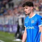 Robin Mirisola in het tenue van KRC Genk langs de zijlijn van een voetbalveld.