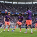Een groep voetballers warmt op met een bal op het veld voor een volle tribune.