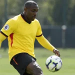 Stefano Okaka tijdens een oefening op een trainingsveld in een geel voetbalshirt.
