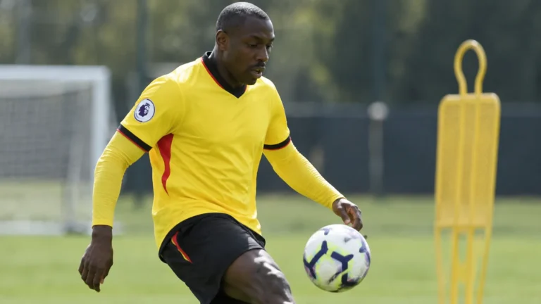 Stefano Okaka tijdens een oefening op een trainingsveld in een geel voetbalshirt.