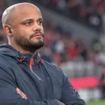 Een Bayern-medewerker in donkere sportkleding met oortje in een stadionomgeving.