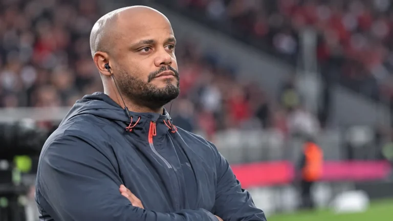Een Bayern-medewerker in donkere sportkleding met oortje in een stadionomgeving.