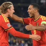 Twee voetballers in rode wedstrijdtenues vieren samen een moment op het veld.