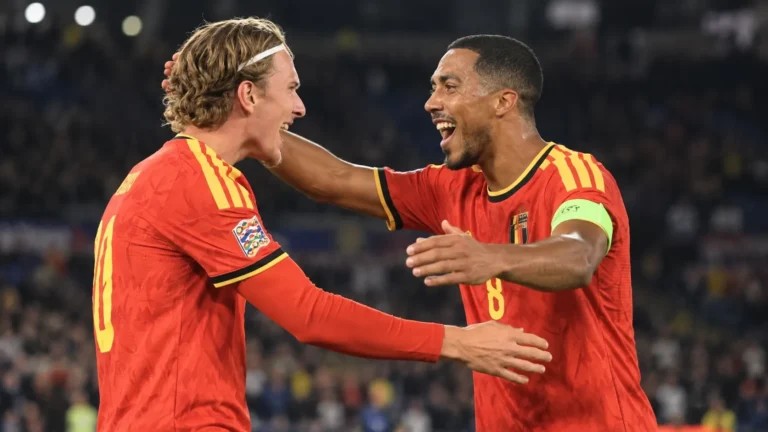 Twee voetballers in rode wedstrijdtenues vieren samen een moment op het veld.